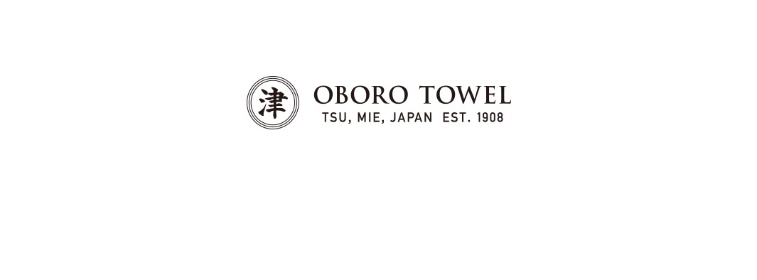 日本桃雪品牌標誌，左側為圓形邊框內含漢字津字，右側排列 OBORO TOWEL TSU, MIE, JAPAN EST. 1908 等品牌資訊，整體呈現深棕色簡約風格。