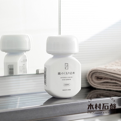 白色塑膠瓶裝著 C-series 鏡面防霧劑，瓶身標有日文「鏡のくもり止」及英文「ANTIFOG LIQUID FOR MIRROR」字樣，並有「浴室專用」和「MADE IN JAPAN」標示。產品瓶蓋為白色圓潤設計，瓶身反射在鏡子中。