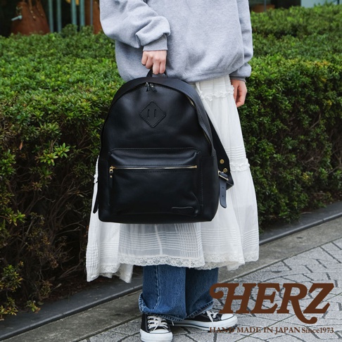 黑色皮革休閒風後背包，配有金色拉鍊和菱形縫線裝飾，由日本品牌 HERZ 製造。