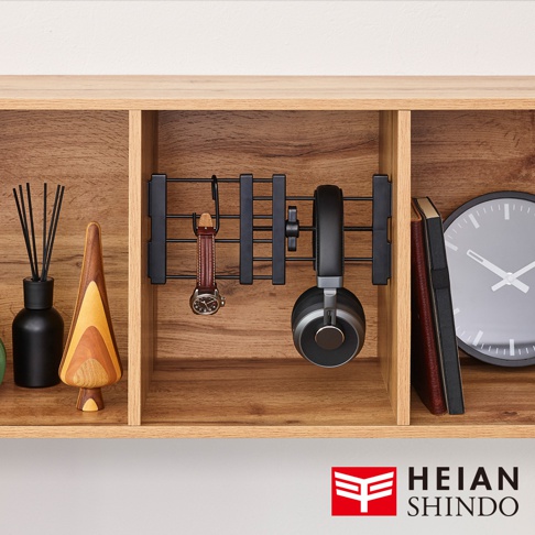 黑色金屬製伸縮縫隙置物架，架上懸掛著一只皮錶帶的手錶和一對黑色耳罩式耳機，置物架固定於木紋層架內。