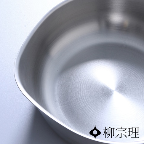 俯視視角拍攝的柳宗理不鏽鋼單手鍋內部，呈現霧面金屬質感，鍋身邊緣具備獨特的弧形導流設計，右下角印有品牌標誌與柳宗理字樣。
