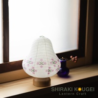 白色紙質提燈，底部為木製圓形底座，燈身飾有粉紅色花朵圖案，線條細緻，整體呈現日式風格。