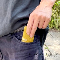 一條黃色MOKU超速乾輕薄吸水小方巾，織紋清晰，一角露出「OM」字樣，被放入深藍色牛仔褲的口袋中。