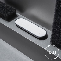 一個橢圓形的白色固體皂，帶有黑色邊框，放置在一個傾斜的灰色平台上。平台旁邊是兩個黑色的粗糙海綿塊。