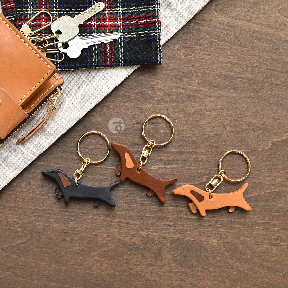 職人手作皮革狗狗造型鑰匙圈，共展示黑色、棕色、淺棕色三款。鑰匙圈造型為臘腸狗，使用皮革製作，搭配金色掛環。