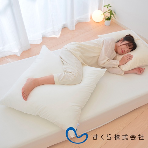 一名女子側臥在白色床墊上，腿部夾著一個白色長方形枕頭，頭部倚靠著另一個較小的奶油色枕頭。