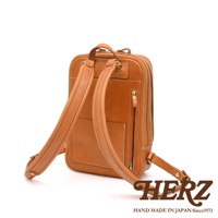 職人手作皮革長方型後背包，呈現經典棕色。包身設計簡潔，配有雙肩背帶，正面有多個口袋，包括一個拉鍊口袋和一個開放式口袋。材質為天然皮革，做工精緻，縫線清晰。