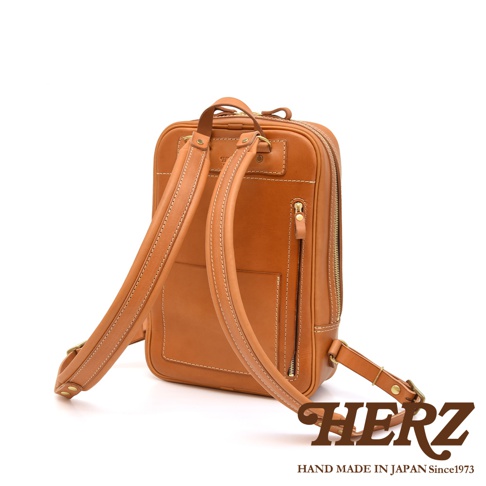 職人手作皮革長方型後背包，呈現經典棕色。包身設計簡潔，配有雙肩背帶，正面有多個口袋，包括一個拉鍊口袋和一個開放式口袋。材質為天然皮革，做工精緻，縫線清晰。