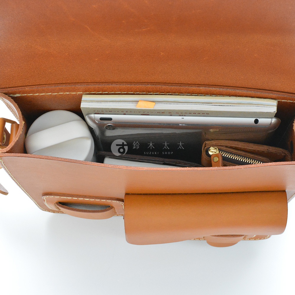 職人手作皮革經典厚實單肩包，棕褐色皮革，包內裝有書本、平板電腦、化妝品、皮夾，展示包款容量。