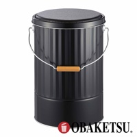 OBAKETSU 品牌標誌旁有一個帶有木製手柄的黑色金屬儲物桶，其桶身有垂直條紋，頂部有蓋子。
