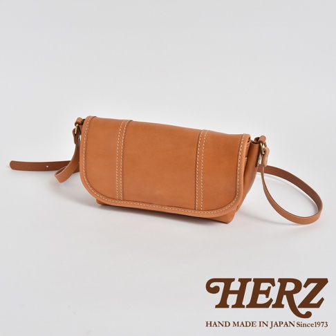 復古風格的棕色皮革郵差包，包身有明顯的白色縫線裝飾，搭配一條細長的皮革背帶，整體呈現簡潔的設計。