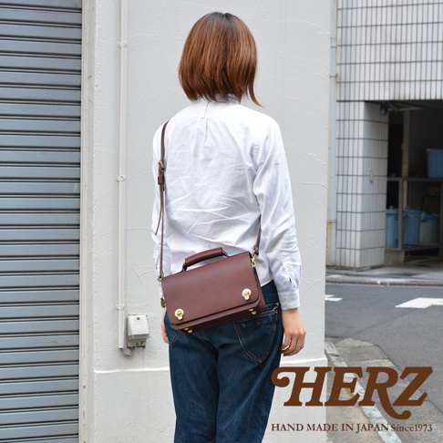 職人手作的經典兩用雙扣迷你單肩包，採用鞣製皮革製成，呈現溫潤的酒紅色。包款設有頂部提把及可調整的斜背帶，雙扣設計增添復古風格，適合搭配休閒服飾。