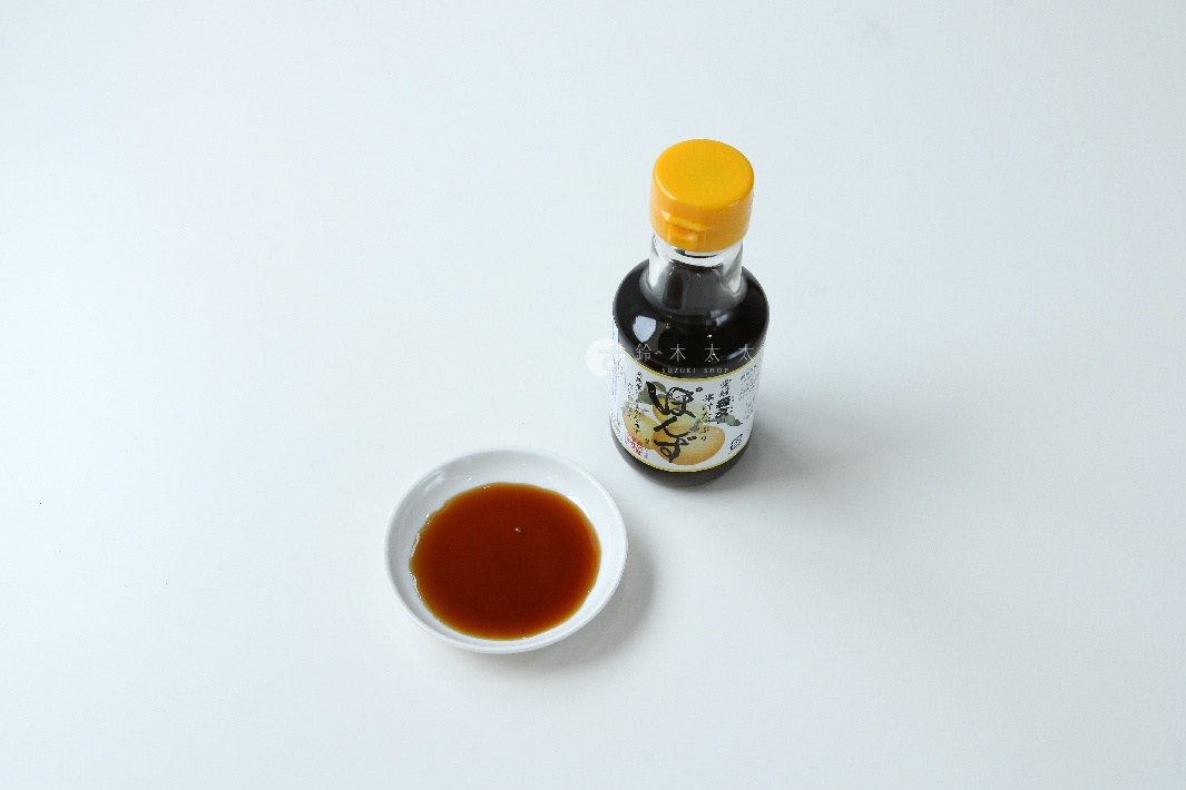 一個150毫升的森文柑橘醋調味料玻璃瓶，瓶蓋為黃色。旁邊有一個白色小碟，裝著深棕色的液體。