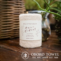 一條淺米色、織紋精緻的有機棉毛巾，標籤上印有日文文字與可愛的棉花圖案，標示「OBORO TOWEL」。