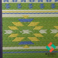 綠色藺草編織的瑜珈墊，帶有黃色、藍色和白色交錯的幾何圖案。