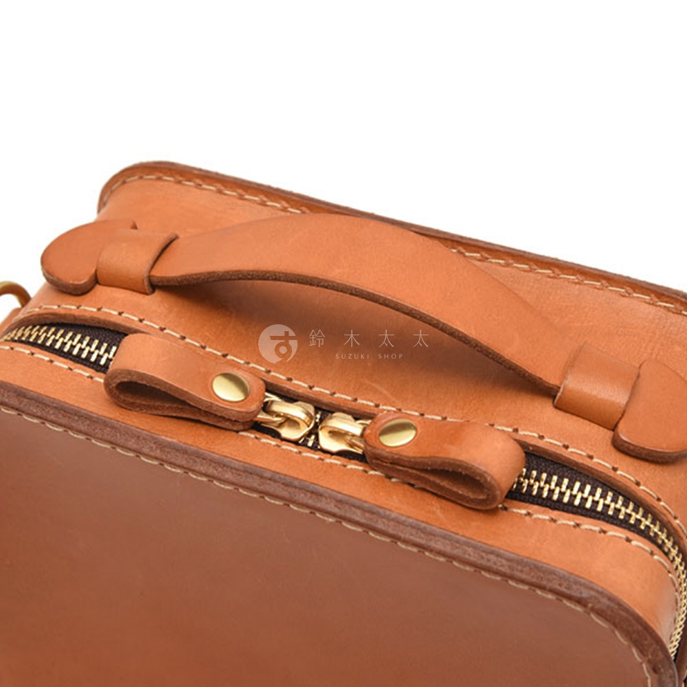 皮革手提包的拉鍊特寫，上面印有日文「鈴木太太 SUZUKI SHOP」字樣。