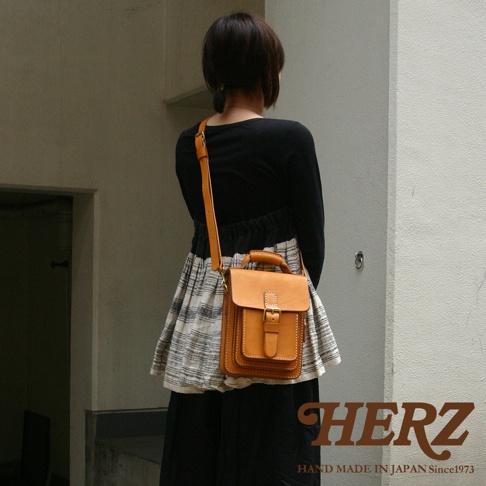 皮革單肩兩用小方包，淺棕色，附有手柄和可調節肩帶，包身有明顯的縫線和金屬釦環。