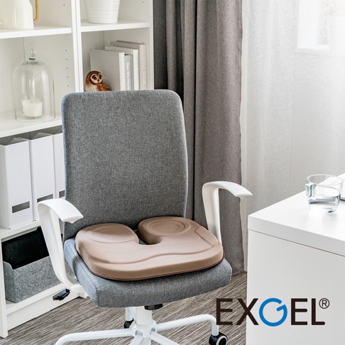 THE OWL Standard U貓頭鷹U字型坐墊，淺褐色，置於灰色辦公椅上，坐墊表面有貓頭鷹圖案，材質為柔軟泡棉，整體呈現舒適的居家或辦公環境。