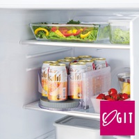 冰箱層架上，一個透明的圓形旋轉收納盤，上面擺放著一排鋁罐飲料，飲料罐為白色和金色，標籤上有日文文字。收納盤旁有一個透明的塑膠飲料架，架內有更多相同飲料。右側有一個透明的玻璃容器，裝有小番茄，容器後方有切塊的黃色和紅色甜椒，以及綠色蔬菜。