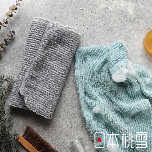 日本桃雪沐浴巾，一條灰色、一條藍色，上面有水珠和泡沫，旁邊有植物和沐浴刷。