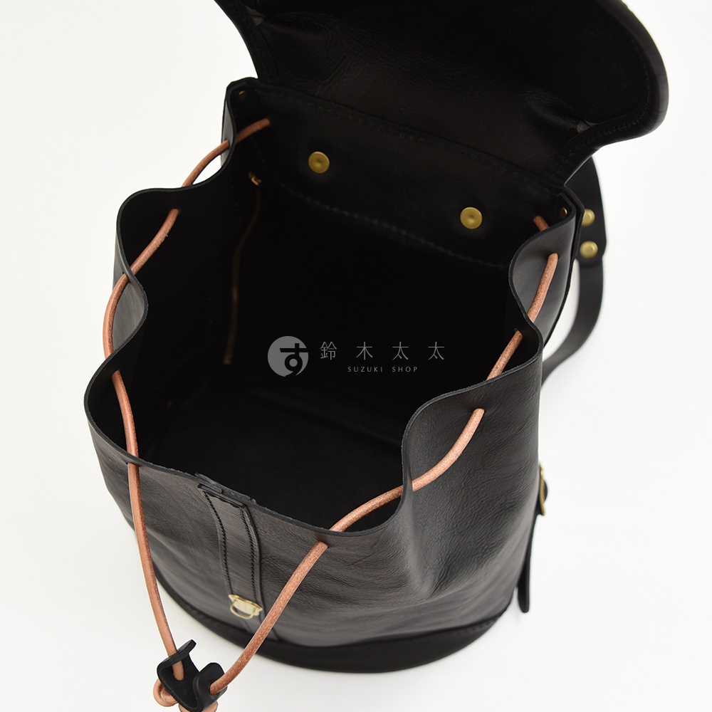 黑色皮革單扣束口後背包，內裡為黑色，束口繩為淺棕色皮革材質，附有金屬扣件。