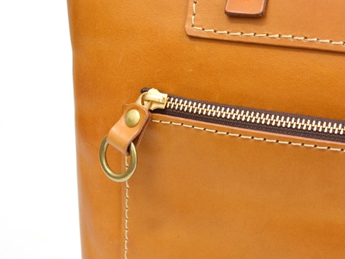 職人手作皮革威靈頓直式拉鍊托特包 (T-151)，特寫展示包款的淺棕色皮革表面，包括一個帶有黃銅拉鍊頭和圓形掛環的拉鍊口袋，以及精緻的縫線細節。