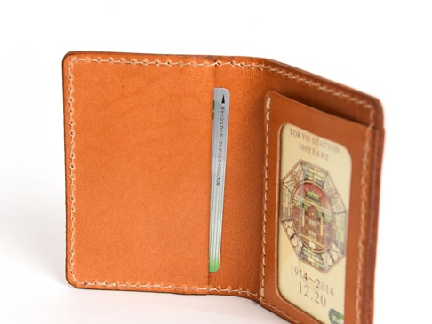 職人手作皮革三面雙折票券收納夾，採淺棕色皮革製成，車縫線清晰。內有卡槽，可放入票券或證件，其中一個卡槽內置印有「TOKYO STATION 100 YEARS」字樣及圖案的卡片。