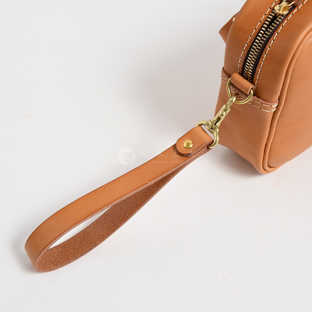棕褐色皮革手提包，配有可拆卸的皮革腕帶和金色金屬扣環，以及黃銅拉鍊，縫線清晰。