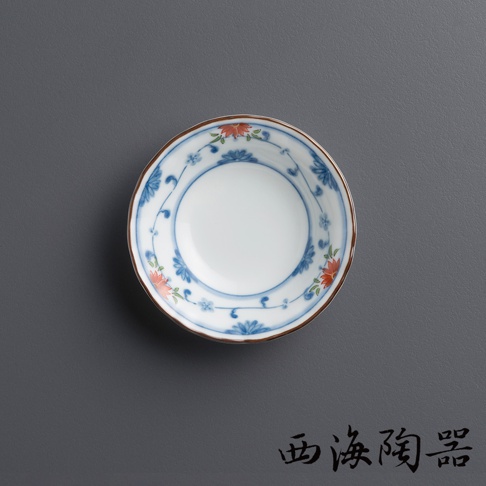 一個陶瓷小圓碟，碟面為白色，邊緣飾有藍色花紋及紅色花朵圖案，碟邊緣處有棕色細線。