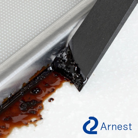 黑色刮刀正在清除帶有黏稠深棕色污垢的銀色金屬邊緣，刮刀邊緣帶有細緻的紋理，背景為白色。