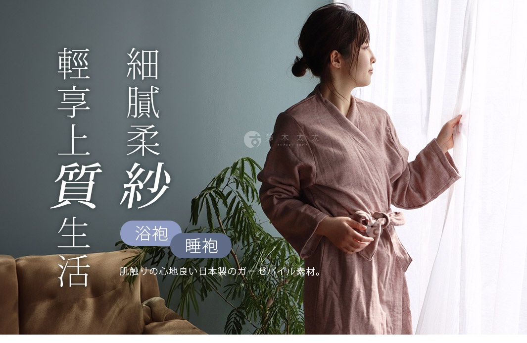 一位女子身穿粉紅色紗質浴袍，浴袍以腰帶繫緊，手觸碰著白色紗簾，背景為灰藍色牆壁與綠色植物。