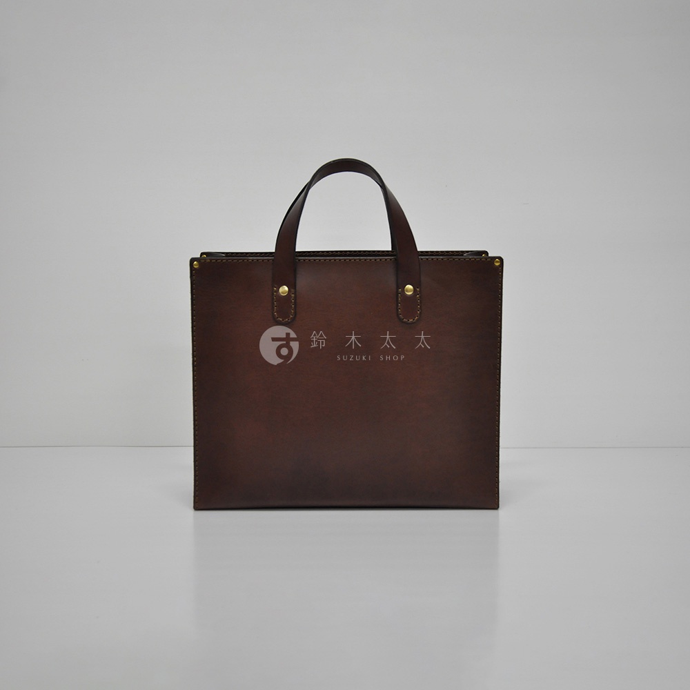 深棕色皮革製成的職人手作直式托特包，具有簡約的設計和兩個提把，包身中央印有品牌標誌。