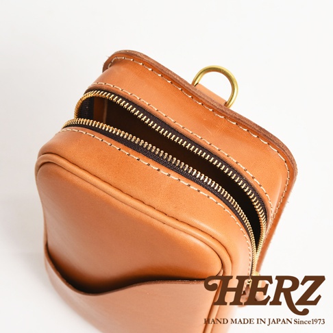 日本HERZ職人手作皮革兩用直立型斜背包，展示了其精緻的皮革工藝和黃銅拉鍊細節，並顯示品牌標誌 HAND MADE IN JAPAN Since1973
