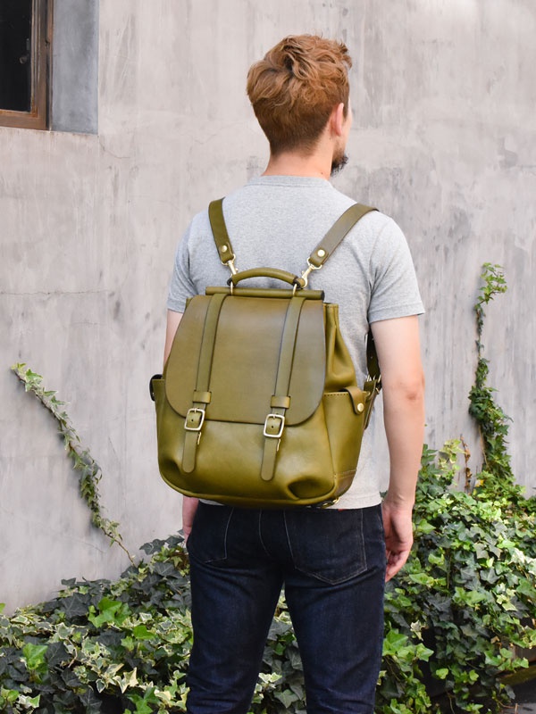 職人手作皮革屋瓦風經典雙扣後背包，橄欖綠色，帶有兩個金屬扣環的翻蓋設計，可調節肩帶。