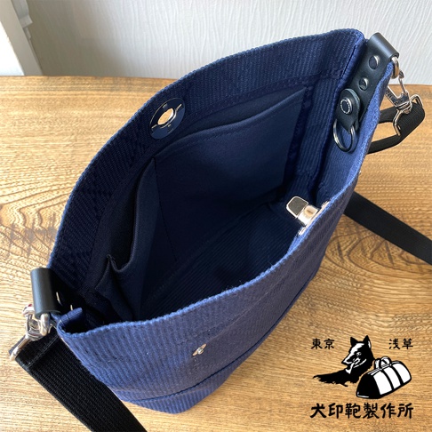 海軍藍刺子織迷你側背包，內有隔層，配有黑色織帶和銀色金屬配件，展現其內裡細節。
