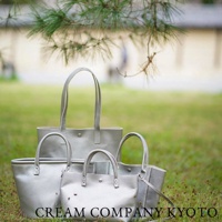 四個銀色手提托特包，大小不同，皆為皮革材質，置於草地上，上方有樹枝。