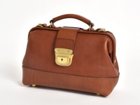 棕色皮革製成的迷你口金包，配有手提把、可拆卸肩帶金屬扣環，以及黃銅色鎖頭和底部腳釘，整體呈現復古醫藥包造型。