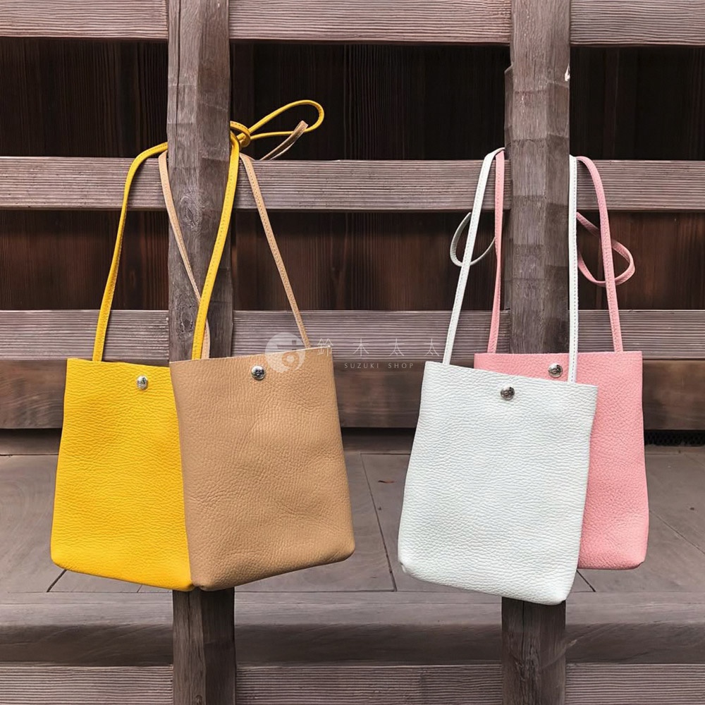 四款京都職人手作隨身手機包，分別為亮黃色、卡其色、淺綠色和粉紅色。包身為荔枝紋皮革材質，設計簡約，帶有長款細肩帶，以金屬釦開合。