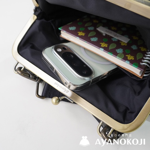 KYOTO AYANOKOJI 標誌出現在復古金屬口金包的底部，包內展示著手機和一本綠葉圖案筆記本。
