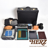 黑色皮革英倫風手提行李箱，內含衣物、文件、相機、錢包、雨傘、護照等旅行用品，搭配棕色皮革零錢包與黃色皮革長夾。