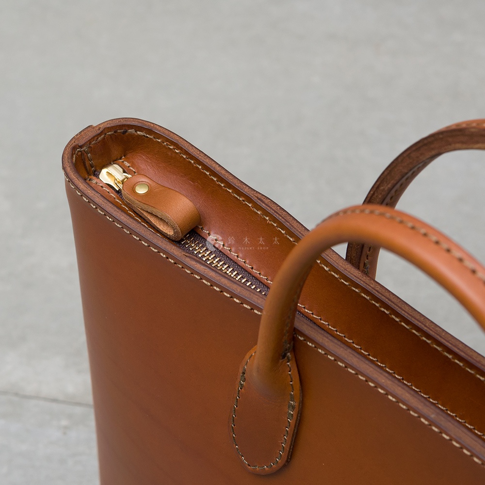 職人手作皮革Organ薄型公事包 G-90，採用棕色皮革製作，設有金色拉鍊及皮革拉頭，手柄處有精緻的縫線。