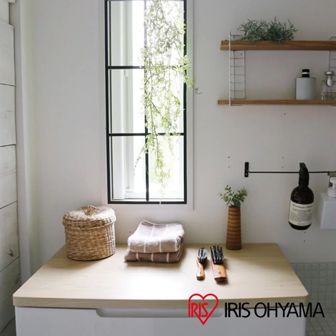 淺木色桌面收納櫃，櫃面擺放著藤編圓形置物籃、疊起的毛巾、兩支木柄刷子，以及一個木製花瓶，櫃子前方有IRIS OHYAMA的Logo。