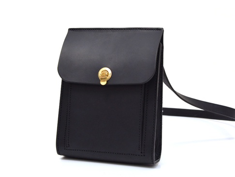 黑色厚實皮革單肩包，配有金色旋轉鎖扣和皮革肩帶。包身線條簡潔，縫線工整，整體呈現復古風格。