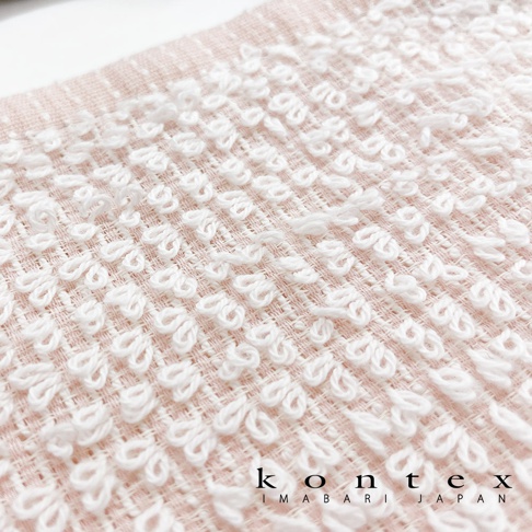 粉色毛巾局部特寫，織有規則排列的白色立體織紋，材質柔軟，呈現細緻的編織紋理。