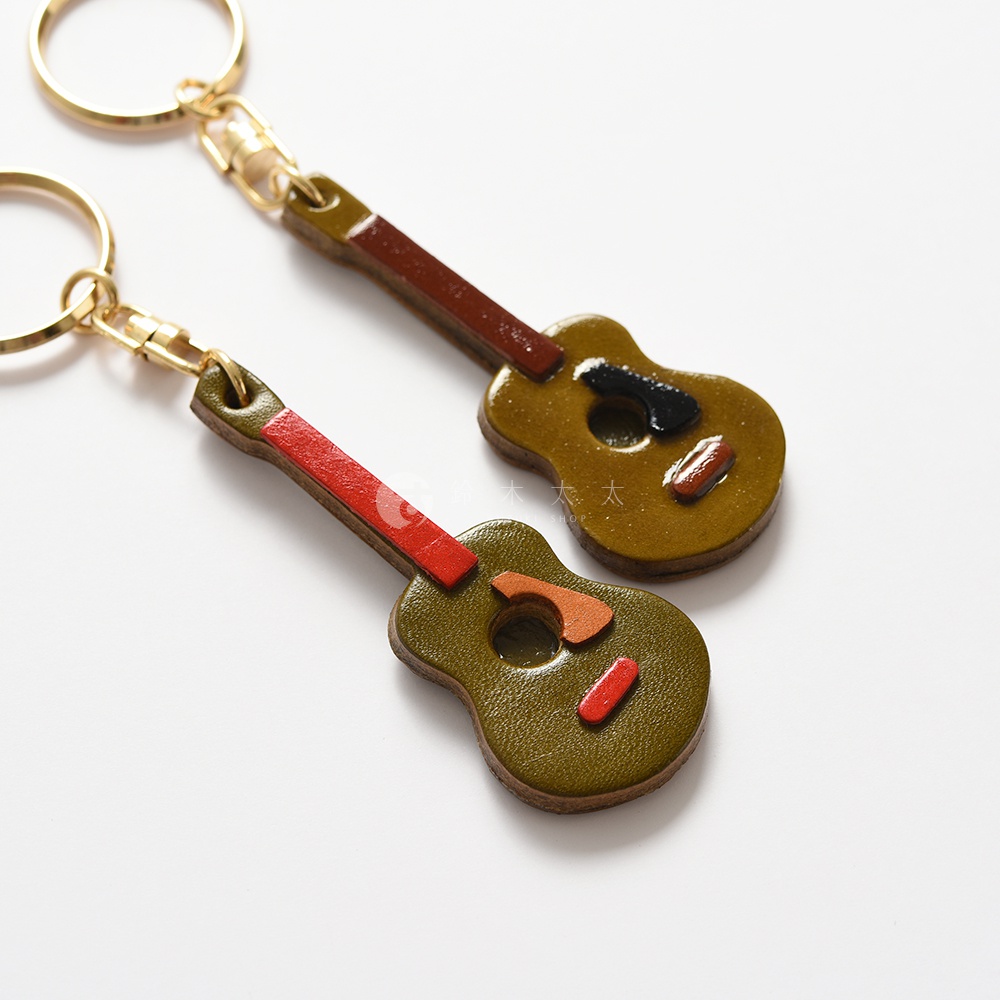 兩個皮革吉他造型鑰匙圈，一個為橄欖綠色，搭配紅色琴頸與橘色、紅色飾條；另一個為淺棕色，搭配深棕色琴頸與黑色、紅色飾條。