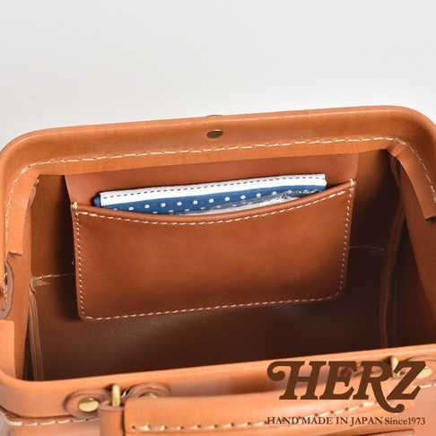 職人手作皮革口金醫生單肩包 CW-12，展示包內頂部視角，淺棕色皮革材質，帶有縫線細節，內部有一個較小的皮革口袋，內有藍白圓點圖案的小物品。