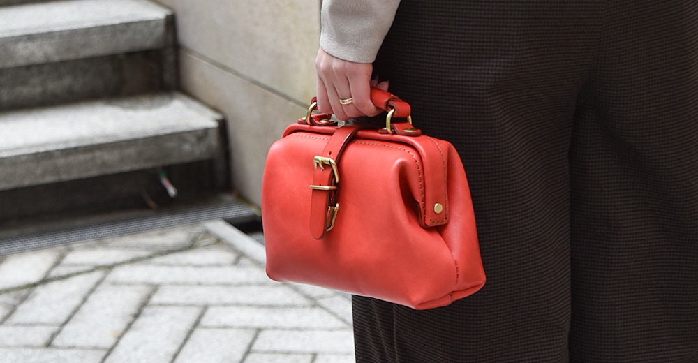 紅色皮革迷你軟皮杜勒斯包，配有金色搭扣和提把，由手部持握。