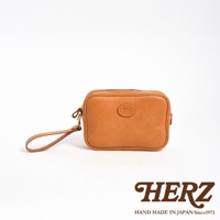 淺棕色皮革手提包，配有可拆卸的皮質腕帶和金屬扣環。包包正面中央有一個橢圓形的皮革標誌，上面壓印有品牌名稱。