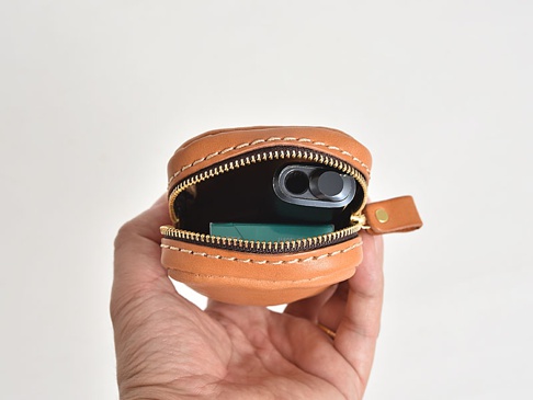 職人手作皮革菸盒收納包，淺棕色皮革，圓形設計，拉鍊開口，內有黑色電子菸裝置及綠色菸盒。