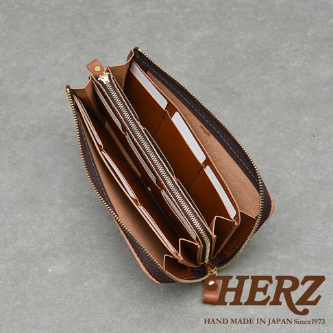 職人手作皮革Organ大容量拉鍊長夾，棕色皮革內裡，多層隔間，拉鍊開合，右下角有HERZ品牌標誌和HAND MADE IN JAPAN Since1973字樣。